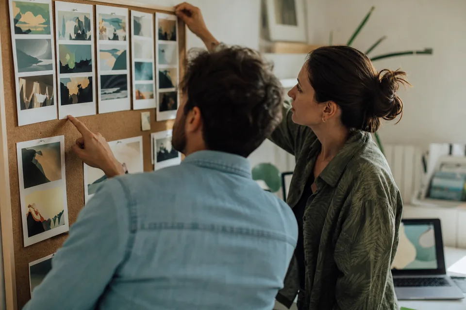 Two marketers review printed vertical video frames pinned to a wall in a small office
