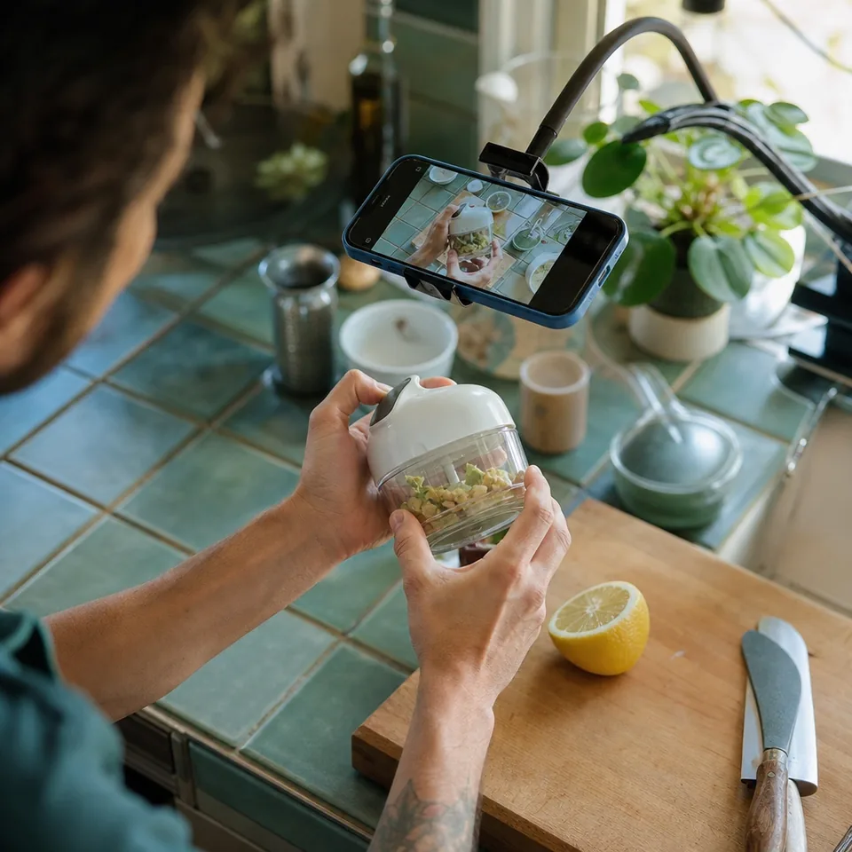 Close shot of hands demonstrating a handheld gadget on a kitchen counter in front of a phone camera
