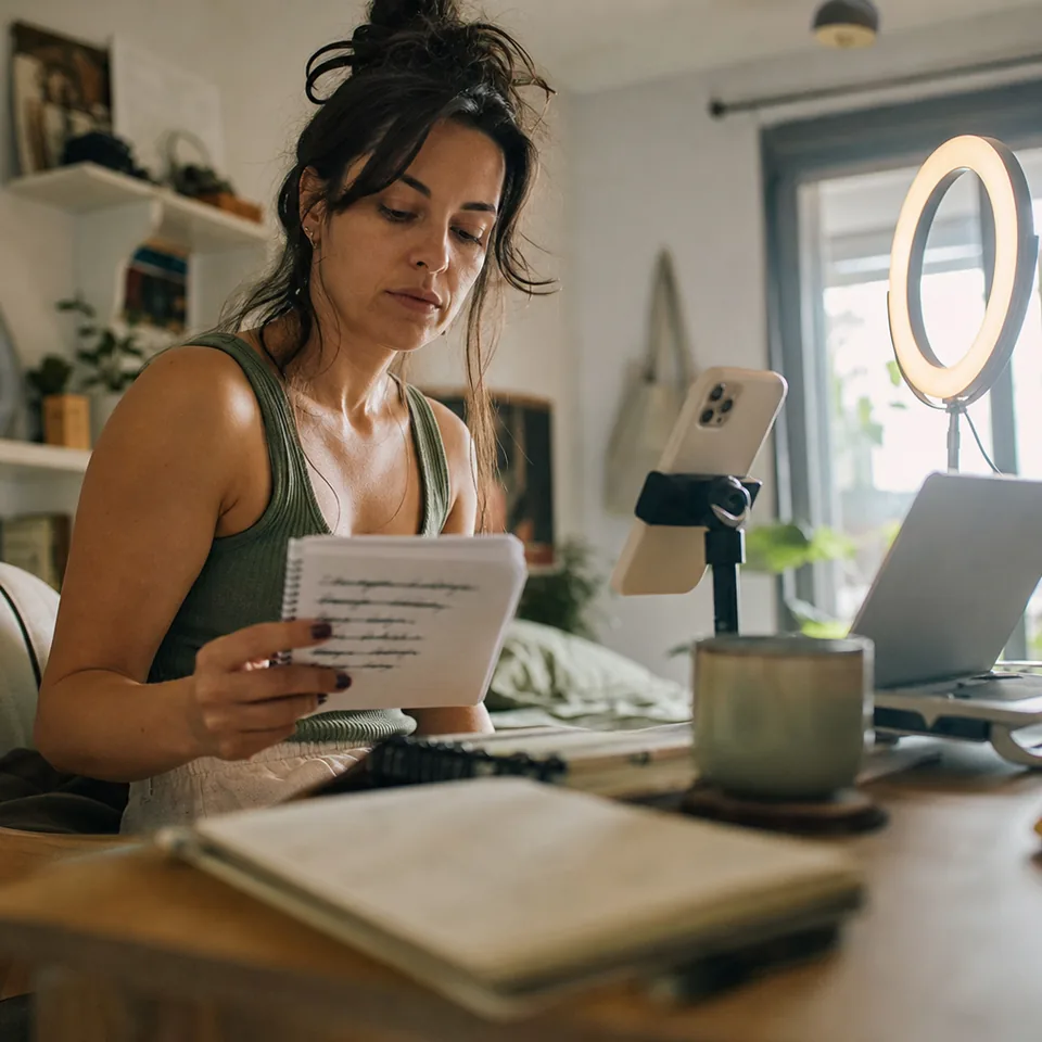 A creator checks a notepad of alternate opening lines beside a phone mounted on a clamp