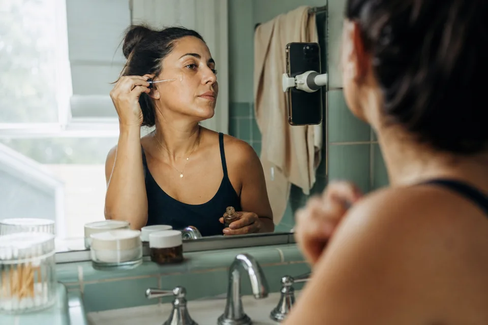 A creator applies moisturizer in front of a bathroom mirror