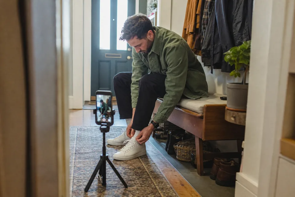 A creator holds a moisturizer jar toward a phone on a stand in a bright bathroom, filming a short ad