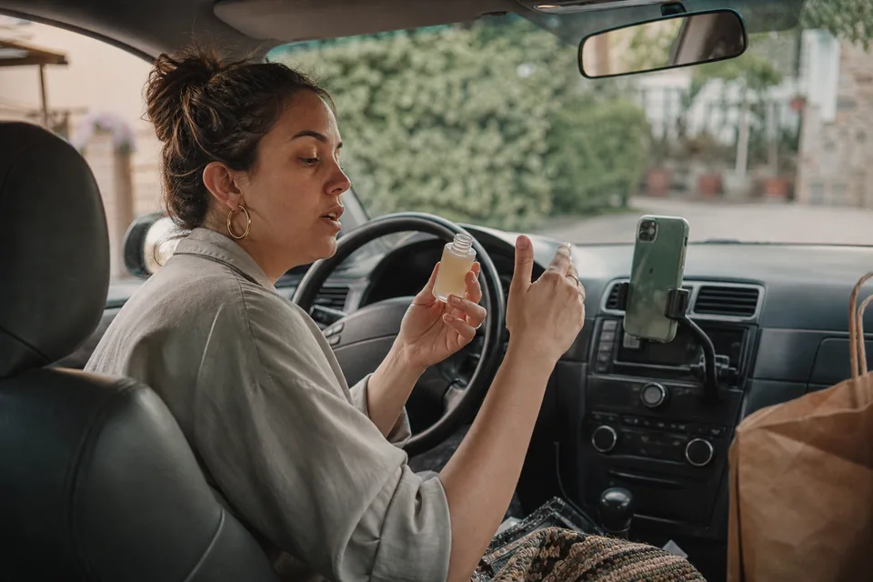 A creator films herself on a phone propped at eye level by a kitchen window, holding a product toward the lens in daylight