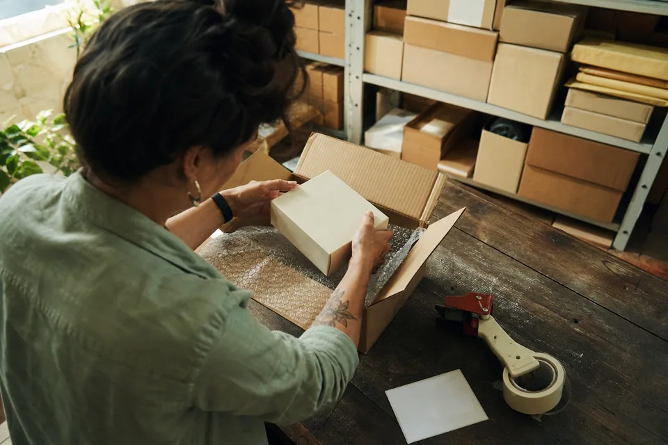Hands packing a product into a shipping box with a tape gun on a workbench